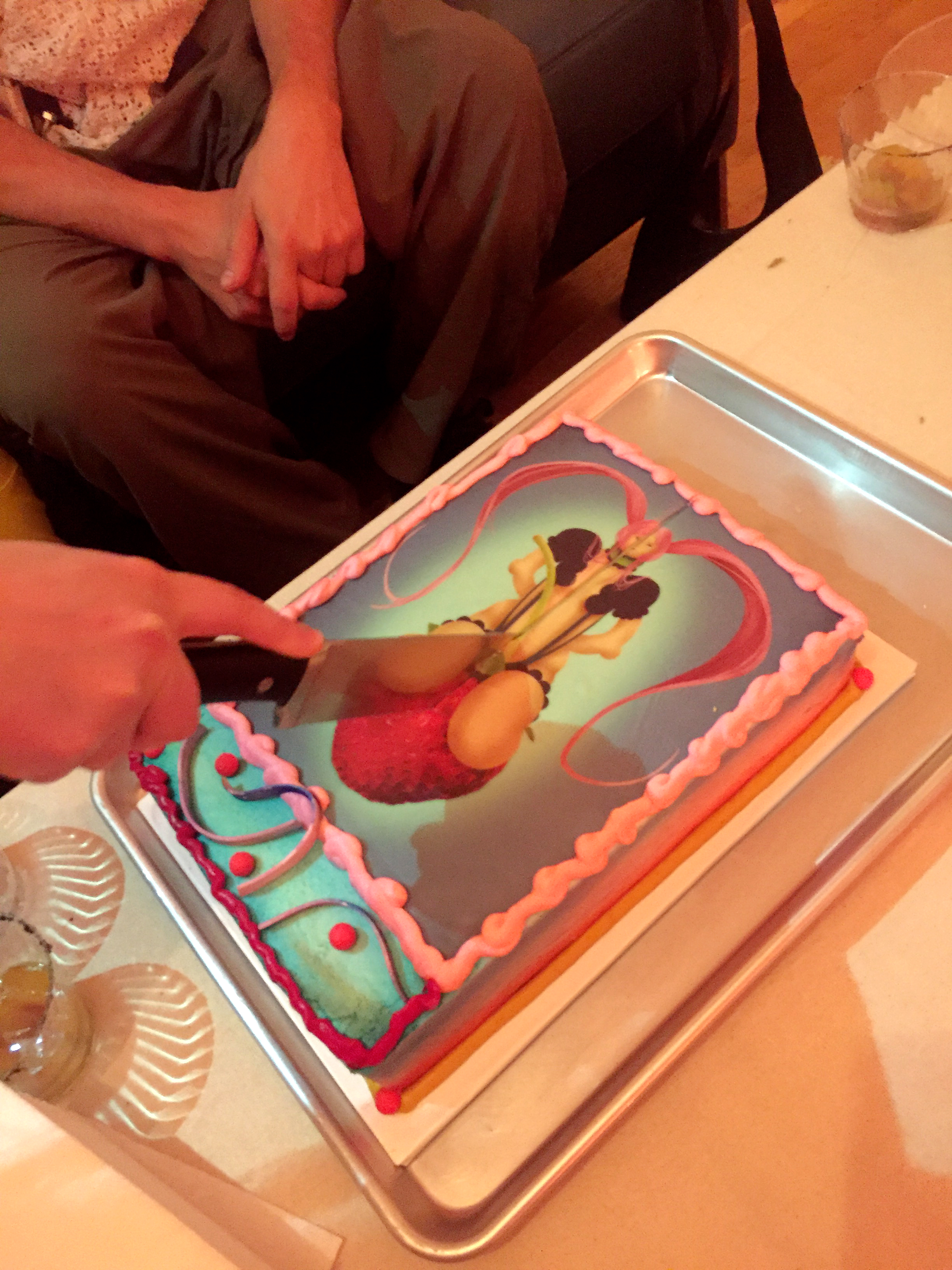 A knife cutting through a cake with an illustration of a girl on it atop a table